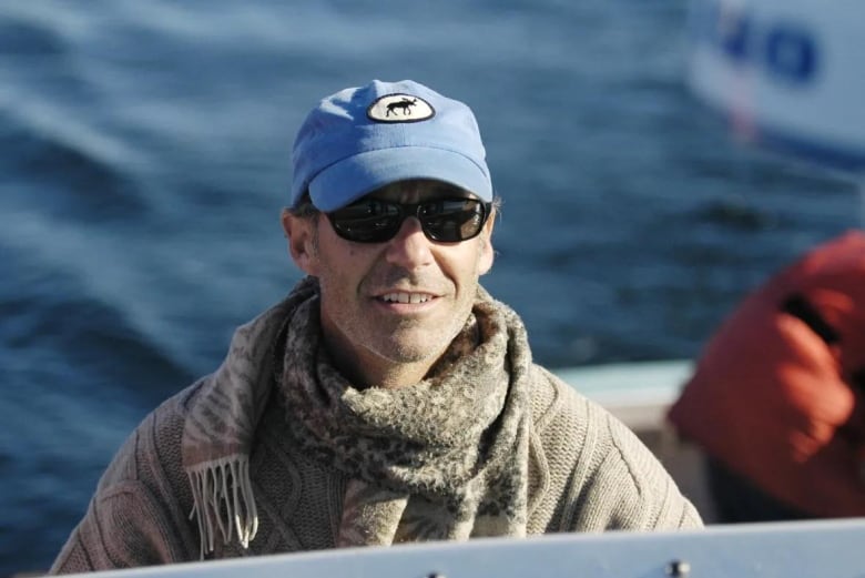 A man wearing a scarf and hat and sweater on a boat in the water