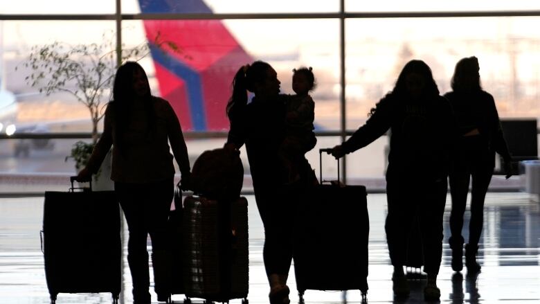 Silhouettes of travellers with suitcases are seen in an airport in front of an airplane. 