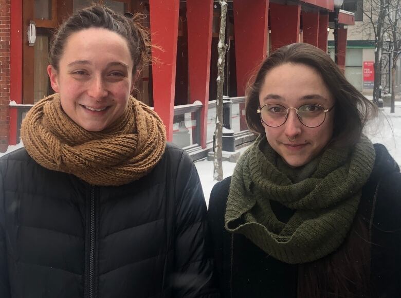 Two women standing next to each other in front of a red building with snow on the ground