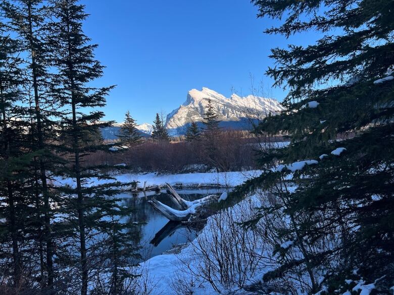 a partly frozen lake is seen with a snow capped mountain in the background 