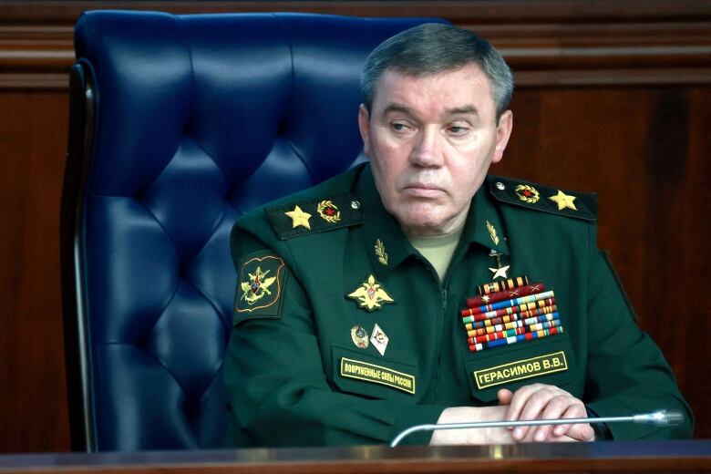 A Russian general in a green military uniform sits in a blue chair.