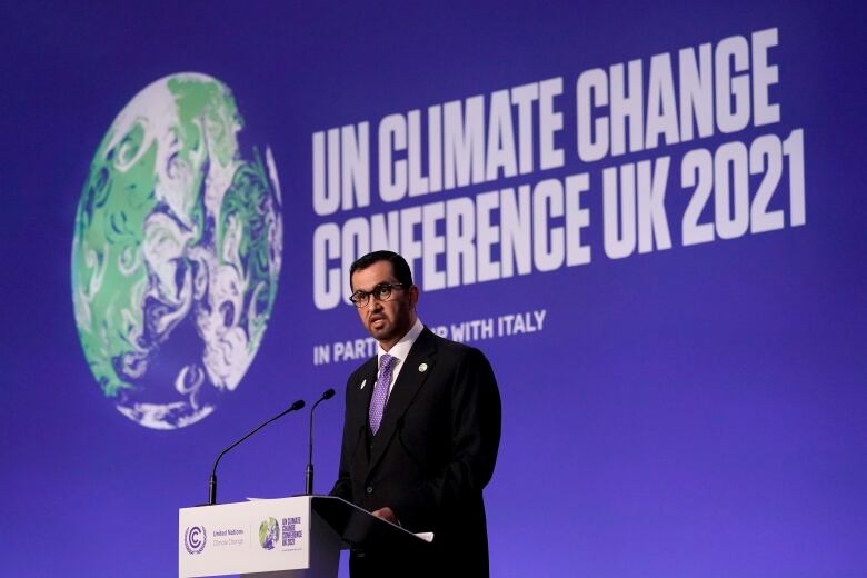 A man stands at a podium delivering an address. Behind him, a banner reads: UN Climate Change Conference UK 2021