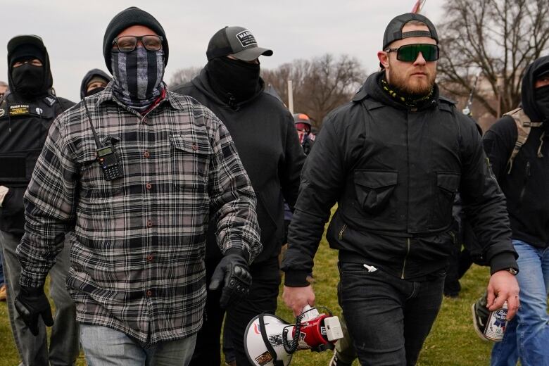 Men are seen walking on grass, one with a megaphone in his hand.