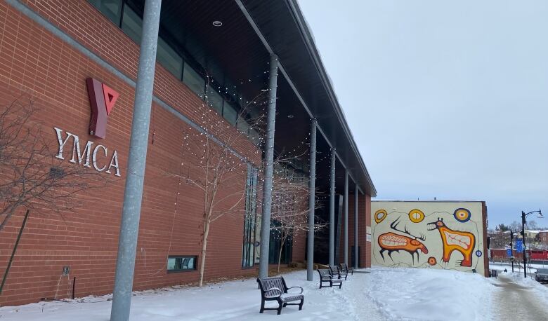 Brick building with YMCA sign in the foreground. Snow on the ground with a mural next to the building in the background. 