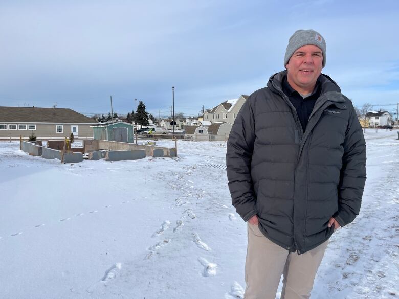 A man in winter attire stand in front of a vacant lot. 