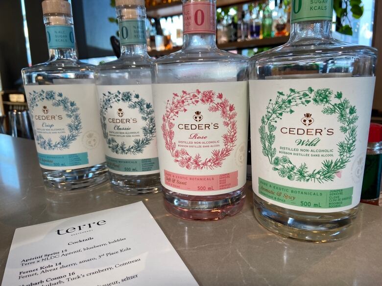 Four bottles of non-alcoholic spirts are lined up along the bar at a restaurant.