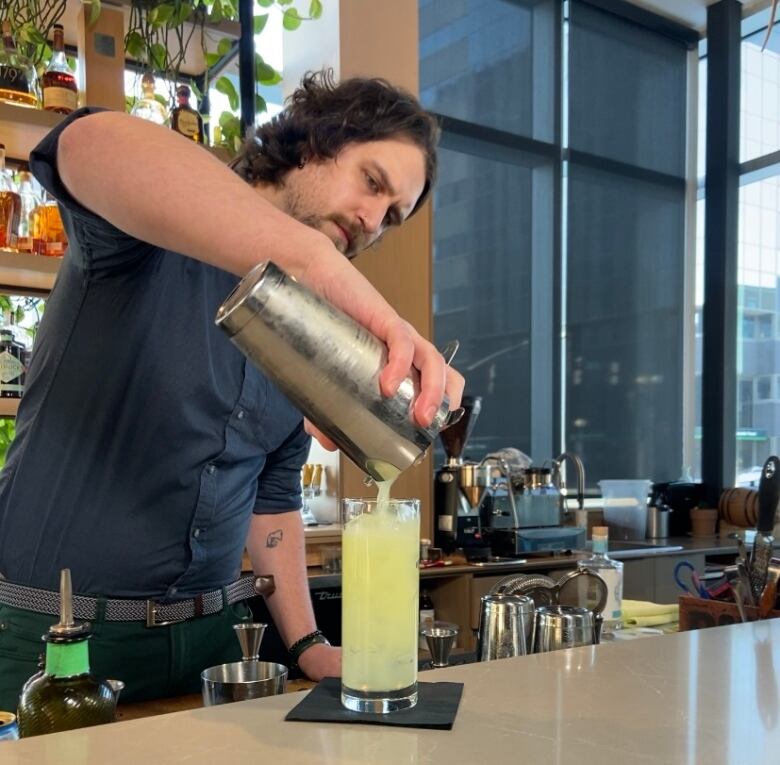 A bartender pours a golden colour drink into a tall glass.