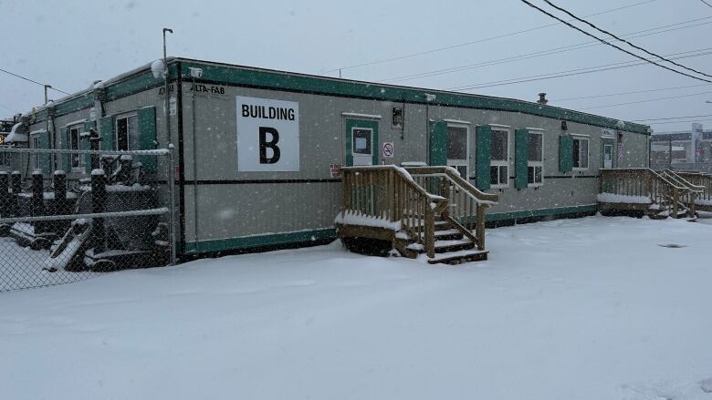 A grey one-storey building made of shipping containers is seen in a snowy landscape. 