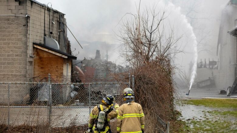 Two firefighters look in the direction of a hazardous waste management company in St. Catharines, Ont., where they're trying to put out a fire.