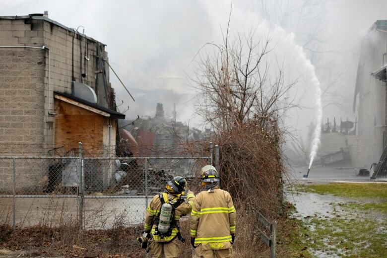 Two firefighters look in the direction of a hazardous waste management company in St. Catharines, Ont., where they're trying to put out a fire.