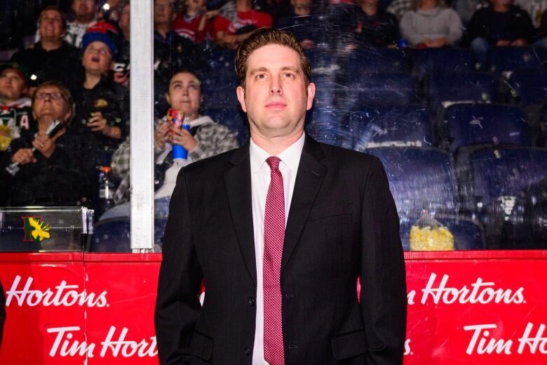 A man in a suit is shown on the bench at a hockey rink.