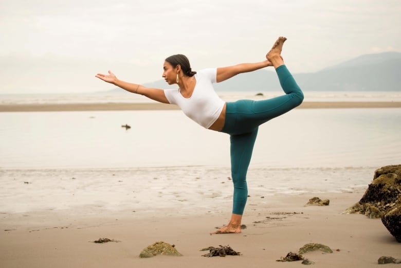 An Indigenous woman stands on a beach, in dancer pose.