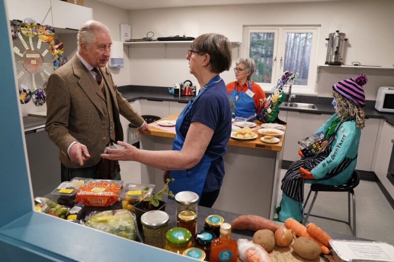 Two people talk in a kitchen as they stand beside food items on a counter.