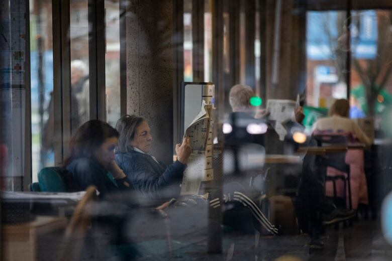 A woman reads a newspaper at a library.