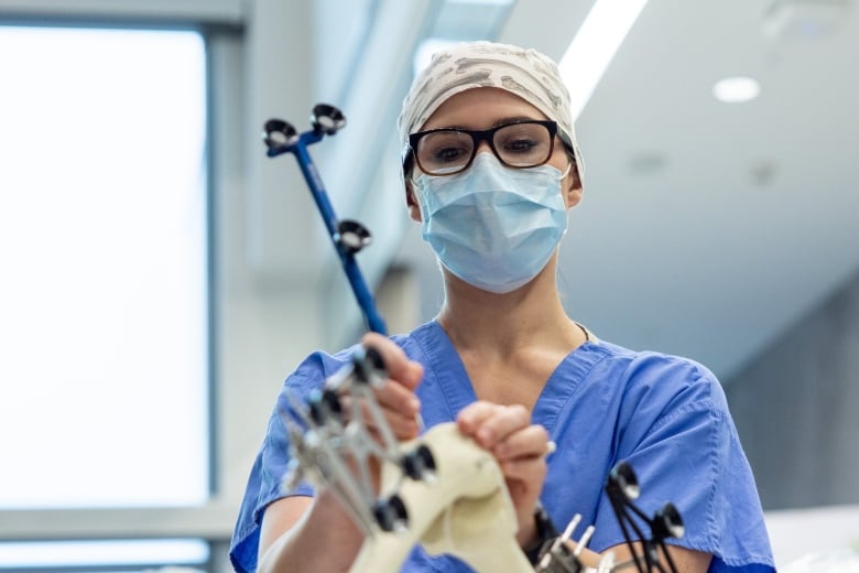 A surgeon holds surgical equipment and demonstrates a hip replacement. 