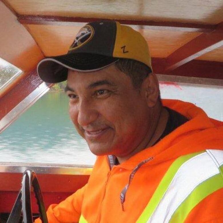 A man wearing a baseball cap and reflective vest smiles at the camera. 