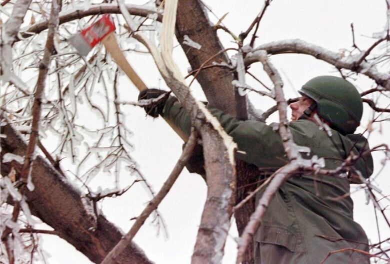 A soldier grimaces as he hacks at a tree with an axe.