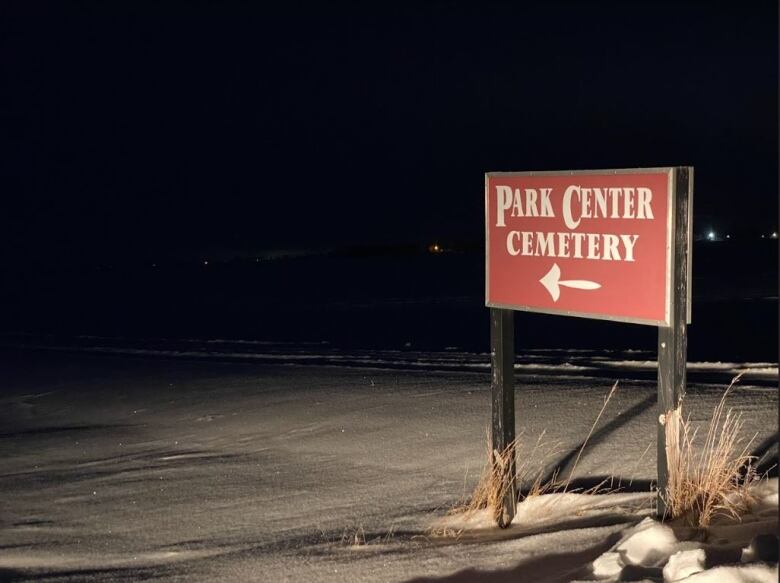 A red sign reading 'Park Center Cemetery' stands tall in a snowy field on a dark night.