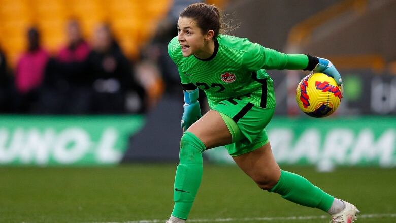 A female soccer goalkeeper rolls the ball forward with her left hand.