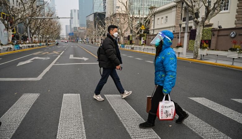 Two pedestrians, both wearing masks, walk in Shanghai, China, in January 2023.