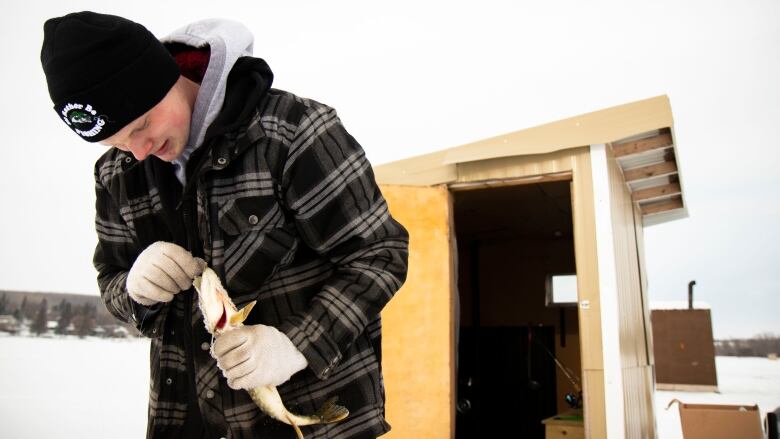 A young man holds a fish he caught ice fishing.