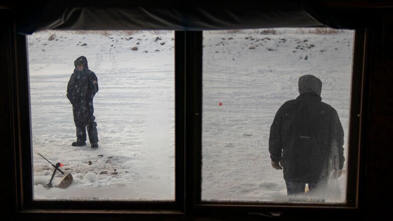 A view of two men ice fishing through a window frame.