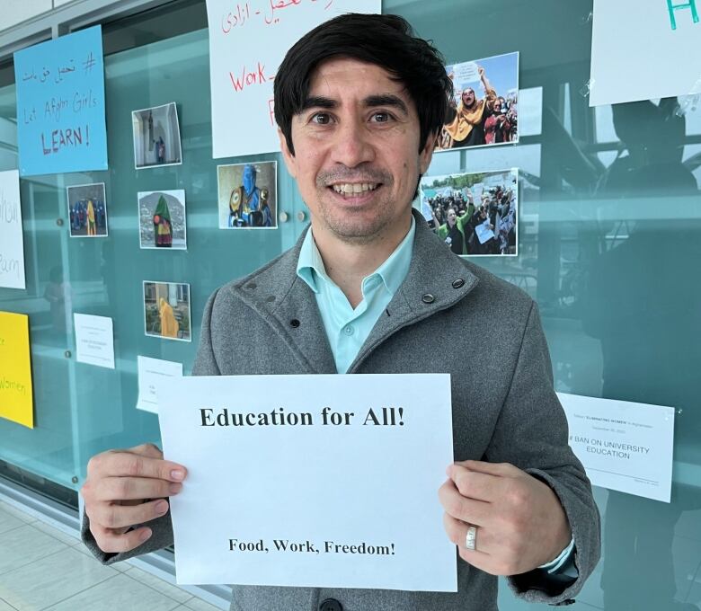 A middle-aged man smiles for the camera. He holds a poster reading 