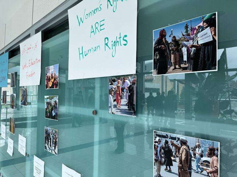 A wall with several posters and photos taped to it. One of the posters reads 