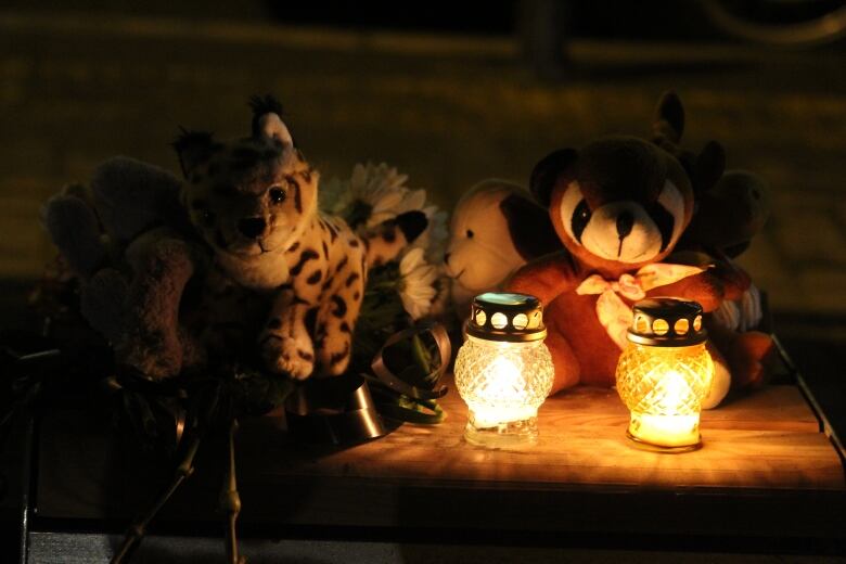 Small stuffed animals are dimly lit by small candles inside glass containers.