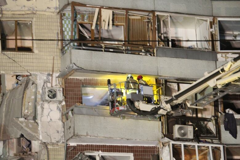 A cherry picker stretches from the right of the photo. There are two firefighters in its bucket, looking into an apartment. 