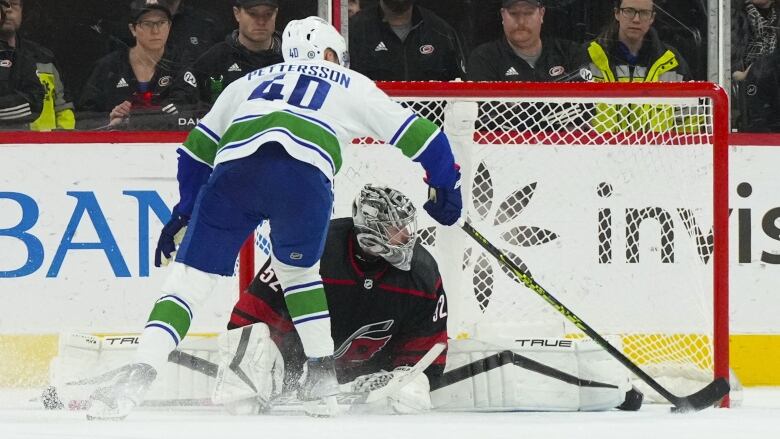 A male ice hockey player scores a goal from close range with the goaltender stretched on his knees.