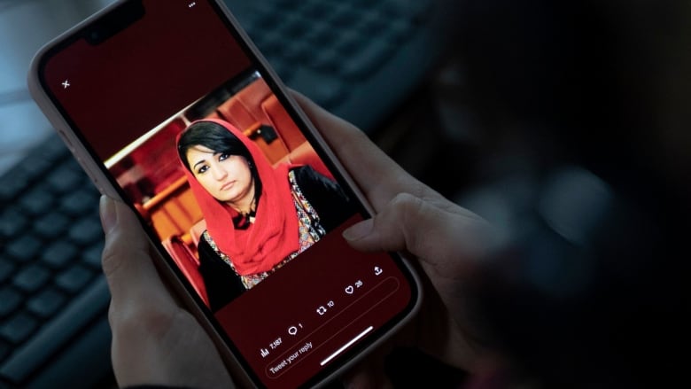 A woman holds a cellphone and looks at a picture of a woman with a red head scarf.