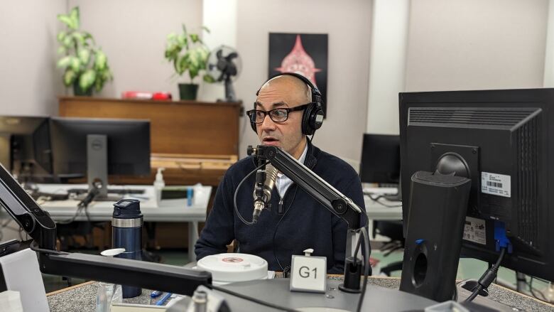 A man wears headphones and speaks into a recording microphone at a desk.