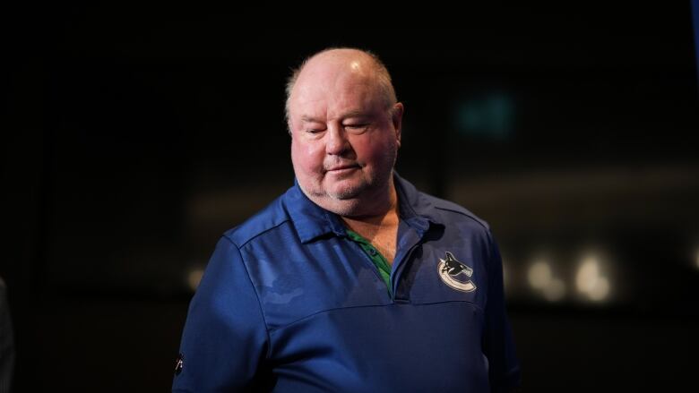 A man wearing a blue Vancouver Canucks sweater walks down a dark hallway.