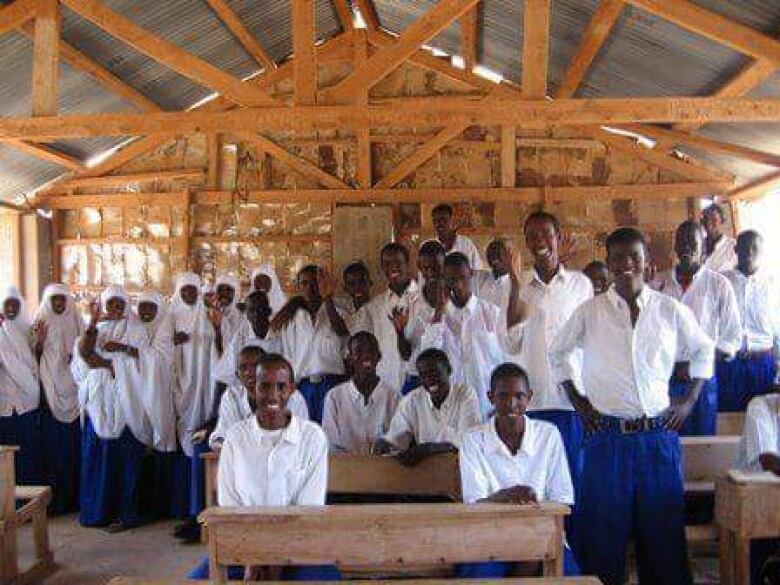 A group of high school students are shown wearing white shirts in a wooden built classroom at the Dadaab refugee camp in Kenya.