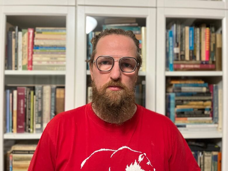 A man in a red shirt stands in front of a book shelf