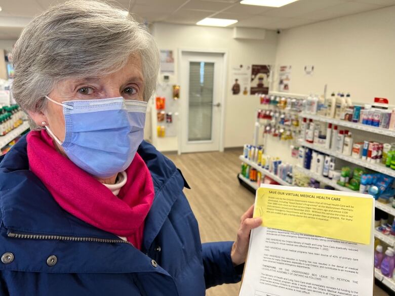 A woman wearing a medical face mask holds up a clip board with a piece of paper asking for signatures.