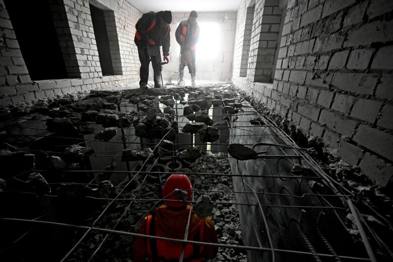 Workers drill and work on the floor inside a concrete building.