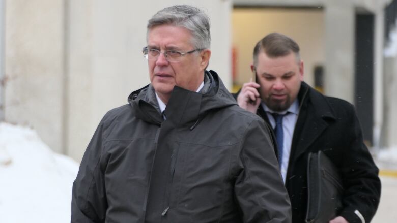 A man in a parka with grey hair is shown above the waste, standing outside on a snowy day.