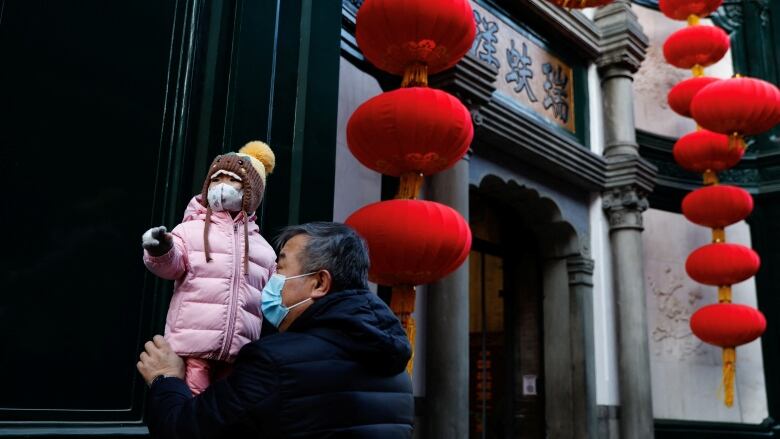 A older man holds a toddler up near bright red lanterns celebrating Chinese Lunar New Year in Bejing.