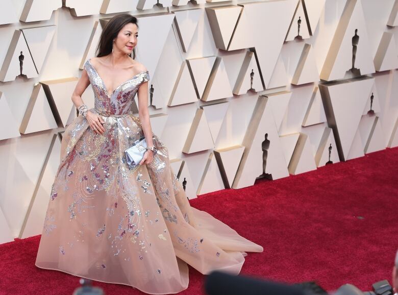 Michelle Yeoh poses on the Oscars red carpet in a silvery flowing gown with a plunging neckline.