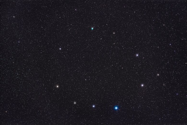 A starry sky is seen with several brighter stars, mainly white with one brilliant blue one, as a semi-circle. At top is a faint green circle, Comet C/2022 E3 ZTF.