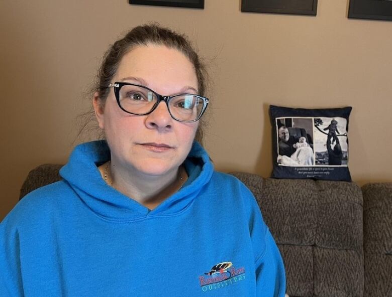 A woman in a blue sweater sits on a brown couch.