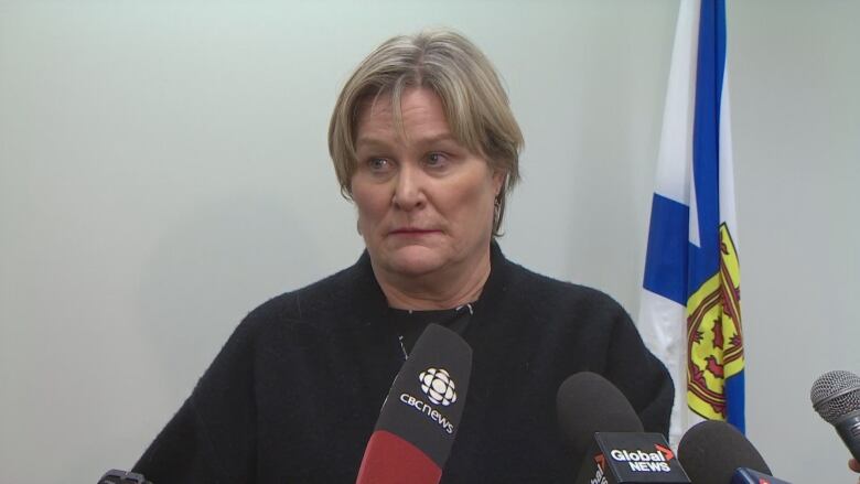 A woman wearing a black sweater stands behind several microphones on a table.