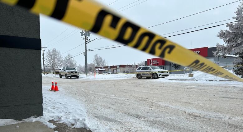 Police cars are seen in the background, while police tape cuts across the frame in the foreground.