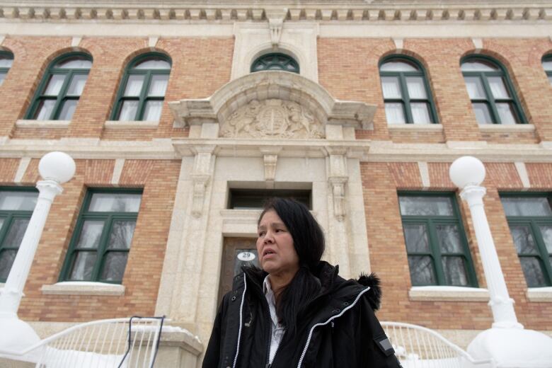 A woman in a black jacket stands in front of a courthouse speaking with reporters.