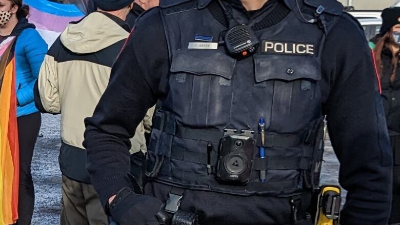 A Calgary police officer's body, with a small pin above his nametag. The pin looks black, with a horizontal blue line running through it.