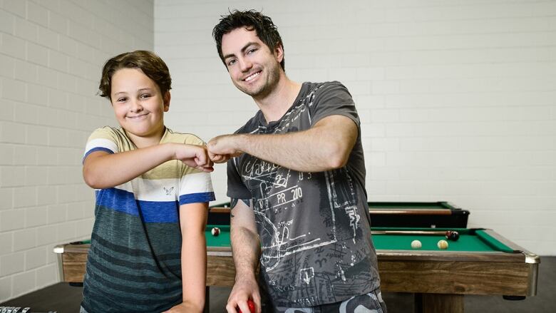 A young boy and a male youth fist bump while playing air hockey. 