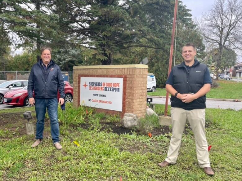 two men standing on either side of a sign for Shephards of Good Hope home