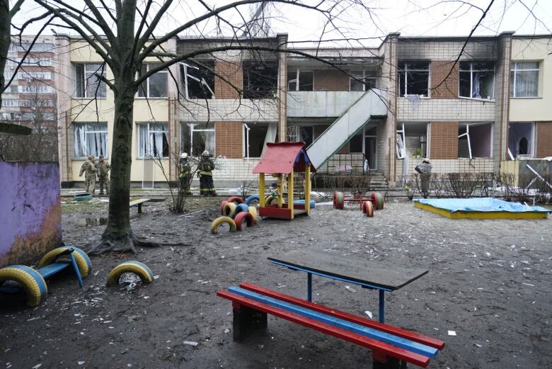 Playground equipment is shown in the foreground, as firefighters inspect a damaged building.